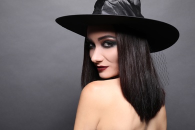 Mysterious witch wearing hat on black background, space for text