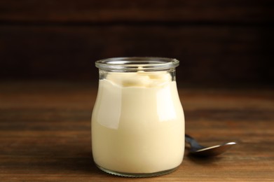 Jar of delicious mayonnaise and spoon on wooden table