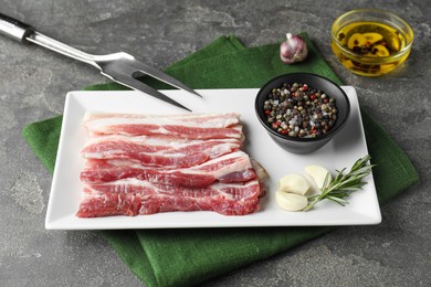 Pieces of raw pork belly, oil, peppercorns, rosemary and garlic on grey textured table