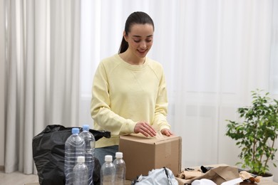 Smiling woman with cardboard box separating garbage in room