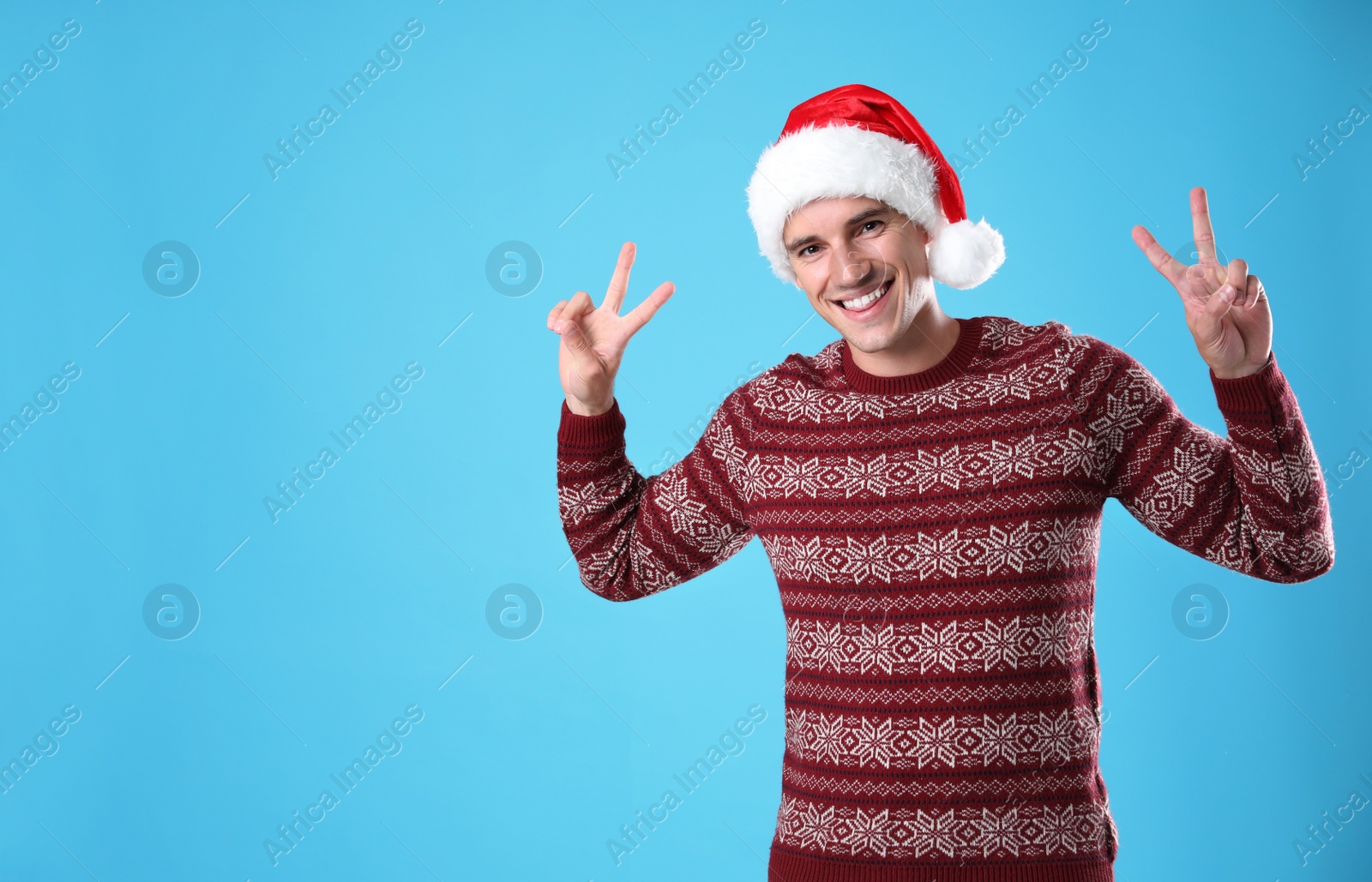 Photo of Portrait of young man in Christmas sweater and Santa hat on light blue background