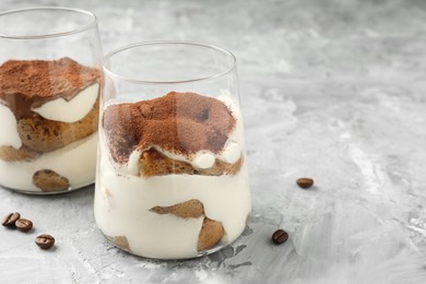 Photo of Delicious tiramisu in glasses and coffee beans on grey textured table, space for text