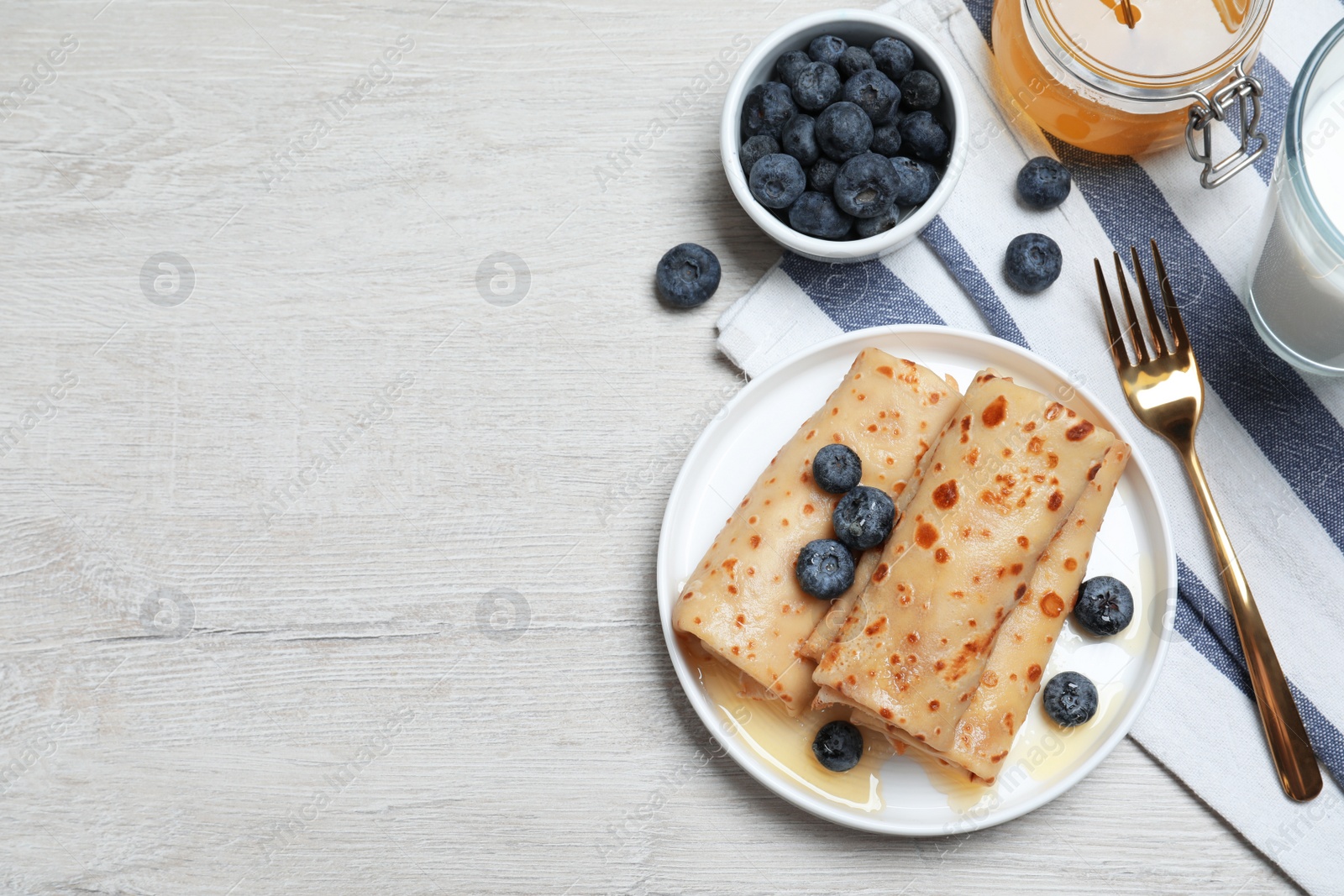 Photo of Delicious crepes served with blueberries, honey and milk on white wooden table, flat lay. Space for text