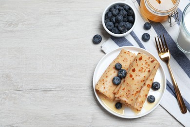 Delicious crepes served with blueberries, honey and milk on white wooden table, flat lay. Space for text