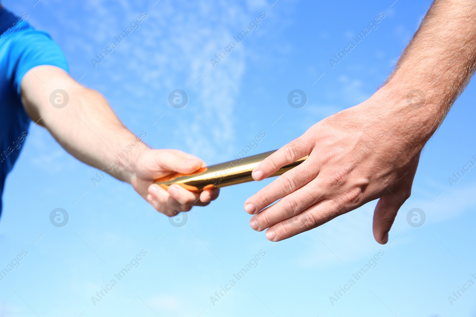 Photo of Man passing baton to his partner against blue sky, closeup