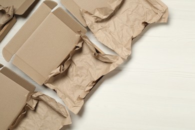Photo of Open cardboard boxes with crumpled paper on white wooden floor, flat lay. Space for text