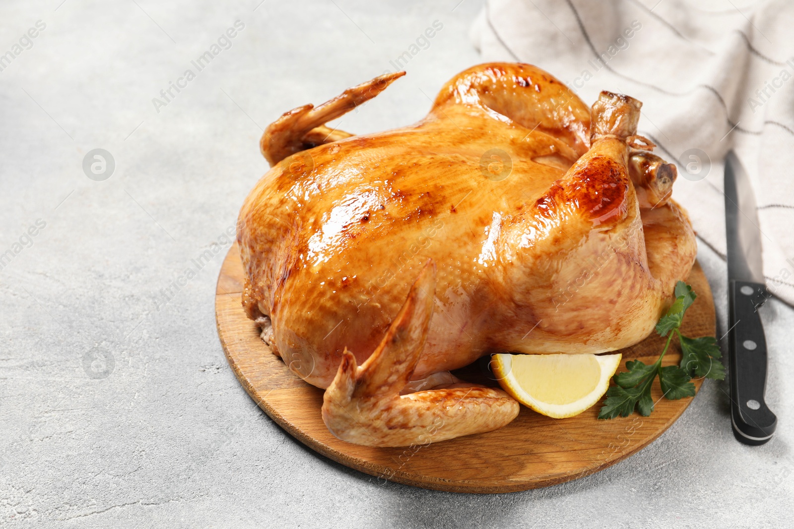Photo of Tasty roasted chicken with parsley, lemon and knife on light grey table