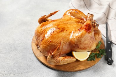 Photo of Tasty roasted chicken with parsley, lemon and knife on light grey table