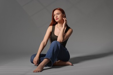 Beautiful young woman sitting on gray background