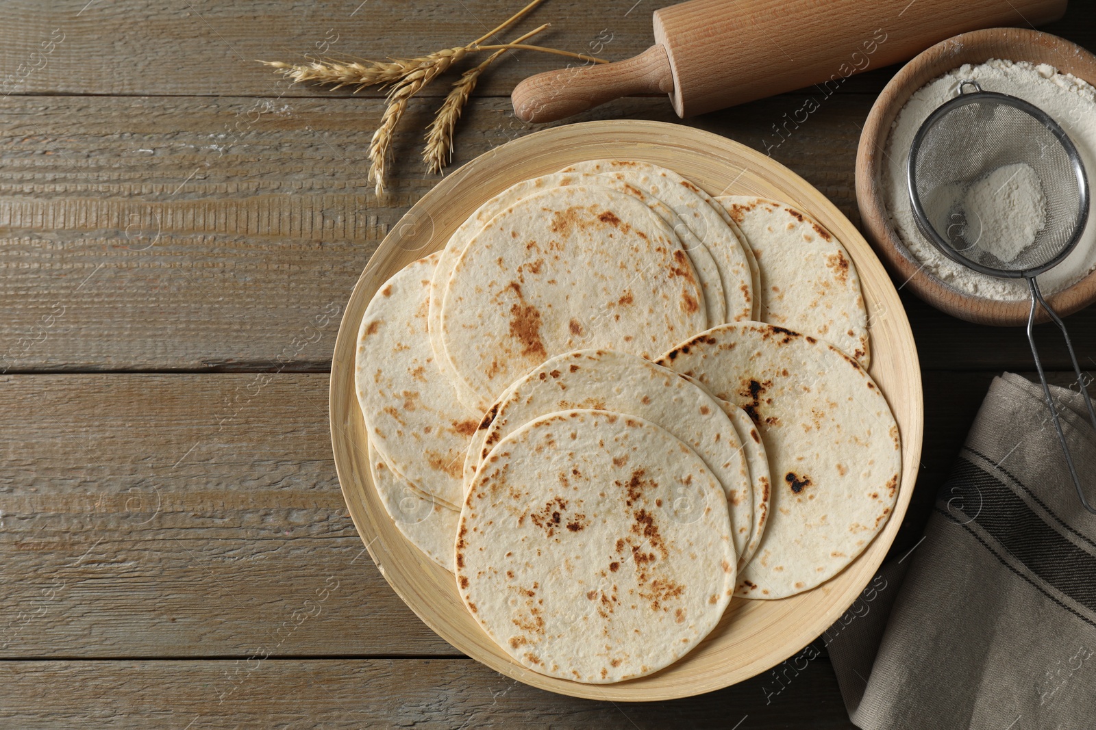 Photo of Many tasty homemade tortillas and rolling pin on wooden table, top view