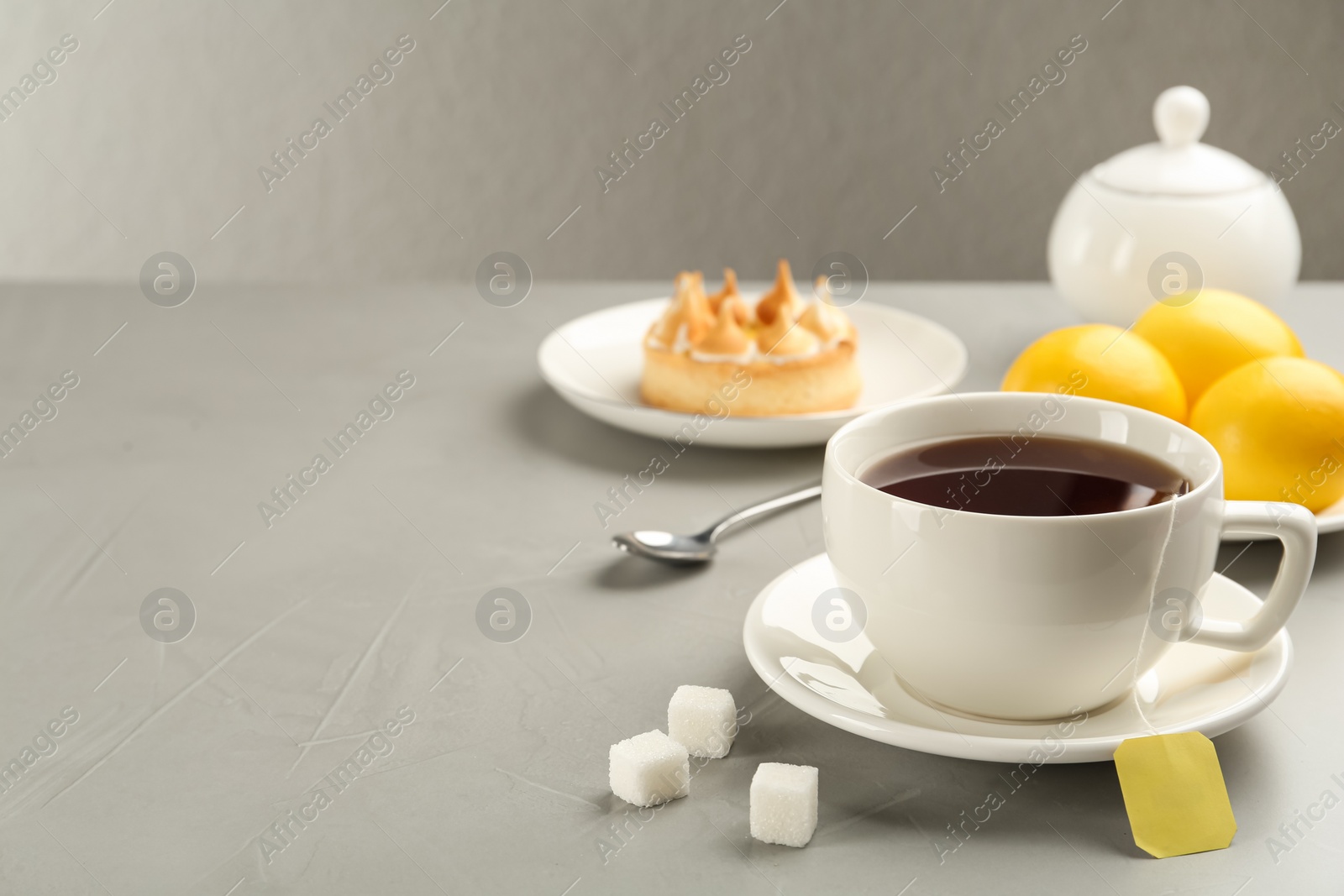 Photo of Tea bag in ceramic cup of hot water and sugar on grey table. Space for text