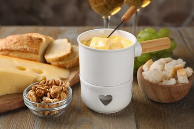 Photo of Pot of tasty cheese fondue and products on wooden table