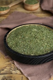 Dried dill in bowl on wooden table, closeup