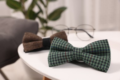 Photo of Stylish color bow ties and glasses on white table, closeup