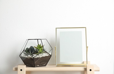 Photo of Florarium with succulent plants and photo frame on table near white wall, space for design. Home decor