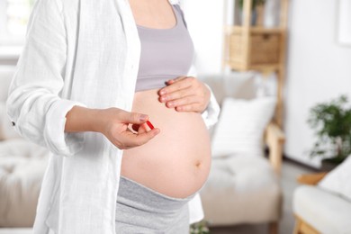 Pregnant woman holding pill at home, closeup
