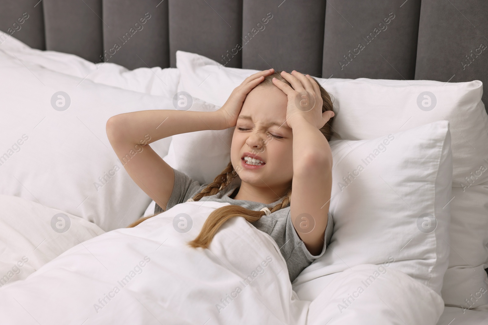 Photo of Little girl suffering from headache in bed