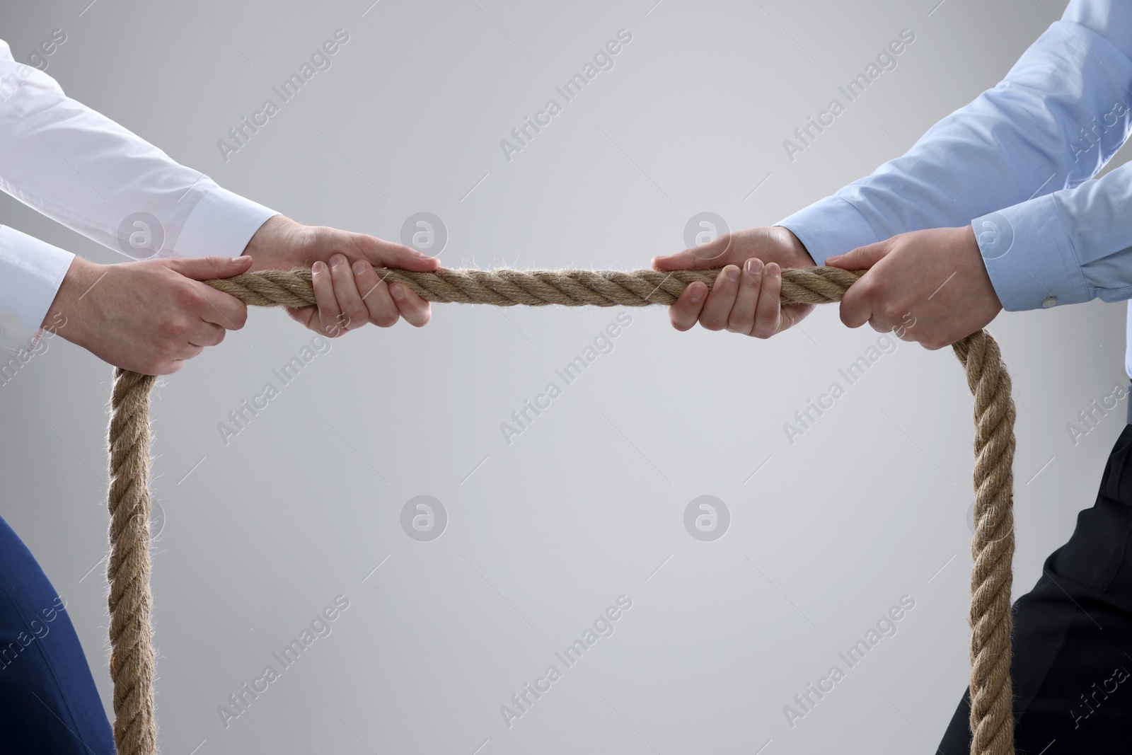 Photo of Dispute concept. Men pulling rope on light grey background, closeup. Space for text
