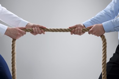 Photo of Dispute concept. Men pulling rope on light grey background, closeup. Space for text