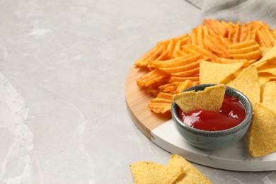 Photo of Tasty ketchup with ridged and tortilla chips on grey table, closeup. Space for text