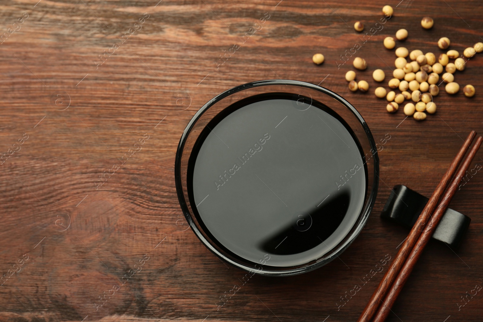 Photo of Soy sauce in bowl, soybeans and chopsticks on wooden table, flat lay. Space for text