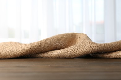 Brown burlap fabric on wooden table, closeup. Space for text