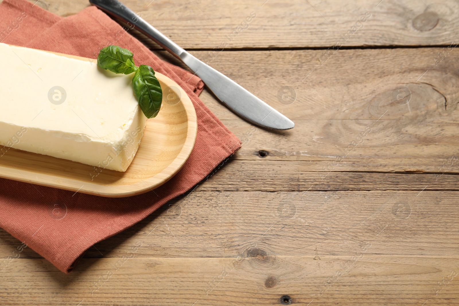 Photo of Block of tasty butter with basil and knife on wooden table. Space for text