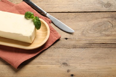 Block of tasty butter with basil and knife on wooden table. Space for text