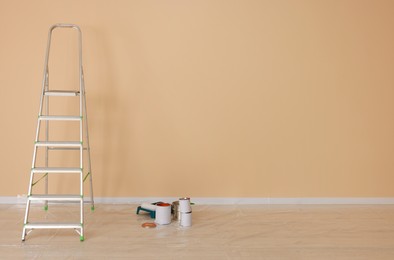 Photo of Metal stepladder near pale orange wall indoors, space for text. Room renovation