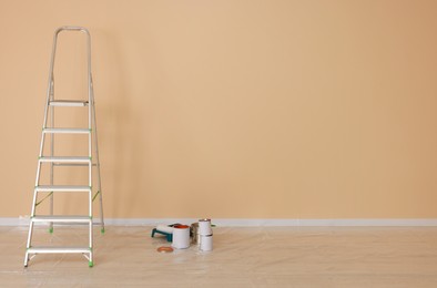 Metal stepladder near pale orange wall indoors, space for text. Room renovation