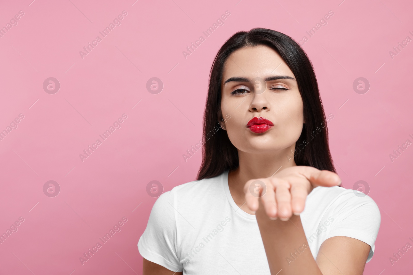 Photo of Beautiful young woman blowing kiss on pink background. Space for text