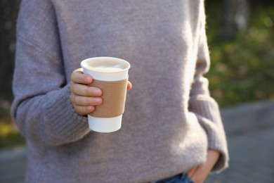 Photo of Woman holding takeaway cardboard cup on city street, closeup. Coffee to go
