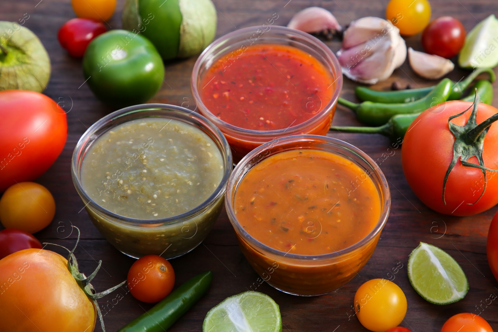 Photo of Tasty salsa sauces and ingredients on wooden table, closeup