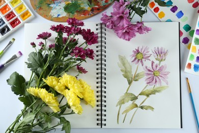 Photo of Painting of chrysanthemums in sketchbook, flowers and supplies on white background, flat lay