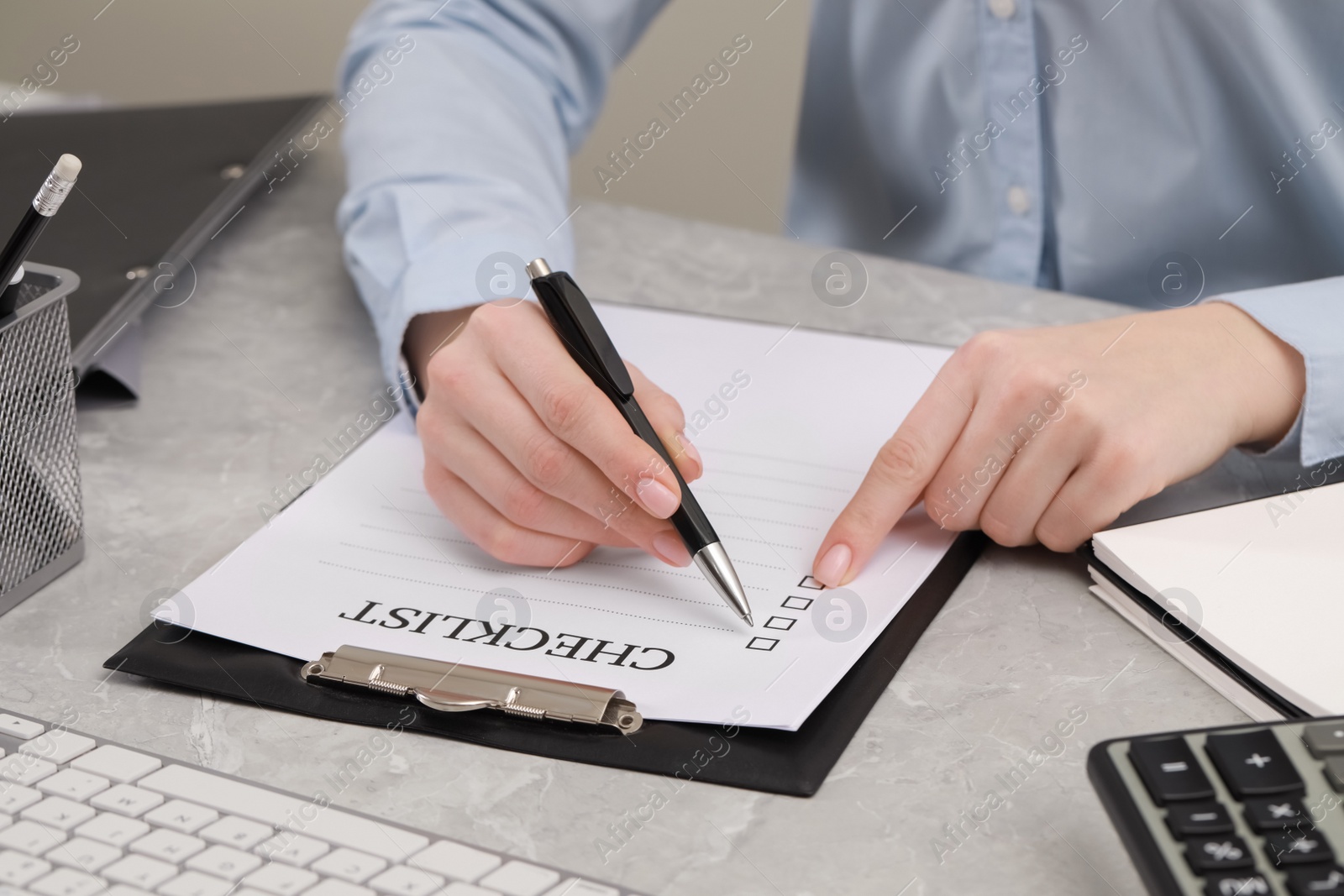 Photo of Woman filling Checklist at grey marble table, closeup