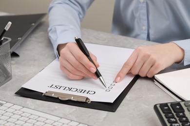 Woman filling Checklist at grey marble table, closeup