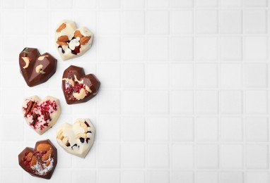 Photo of Tasty chocolate heart shaped candies with nuts on white tiled table, flat lay. Space for text