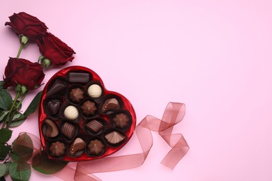 Photo of Heart shaped box with delicious chocolate candies, roses and ribbon on pink background, flat lay. Space for text