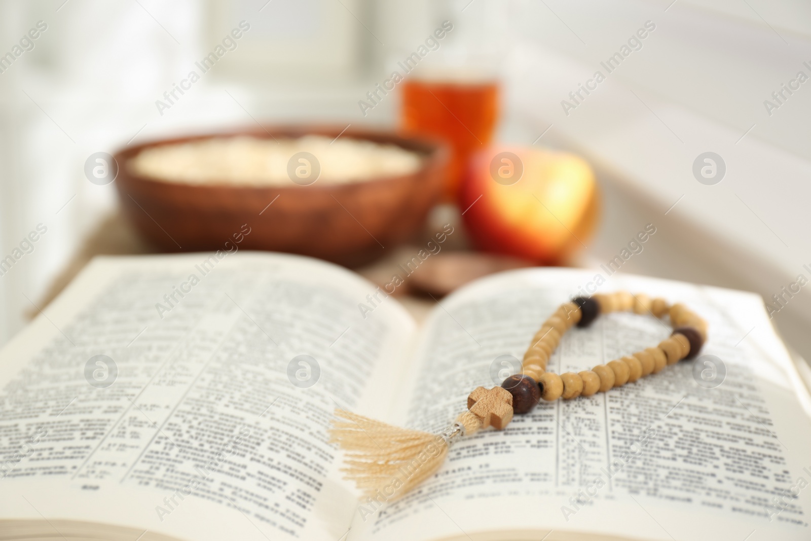 Photo of Holy Bible with prayer beads on window sill indoors, closeup. Great Lent season