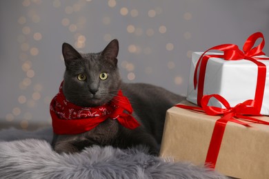 Cute cat in bandana on faux fur near gift boxes indoors