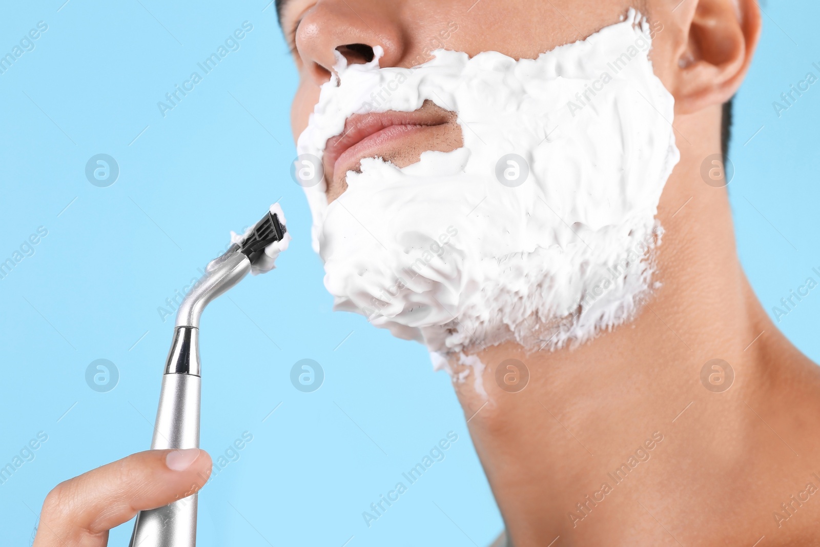 Photo of Young man shaving on color background, closeup