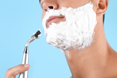 Young man shaving on color background, closeup