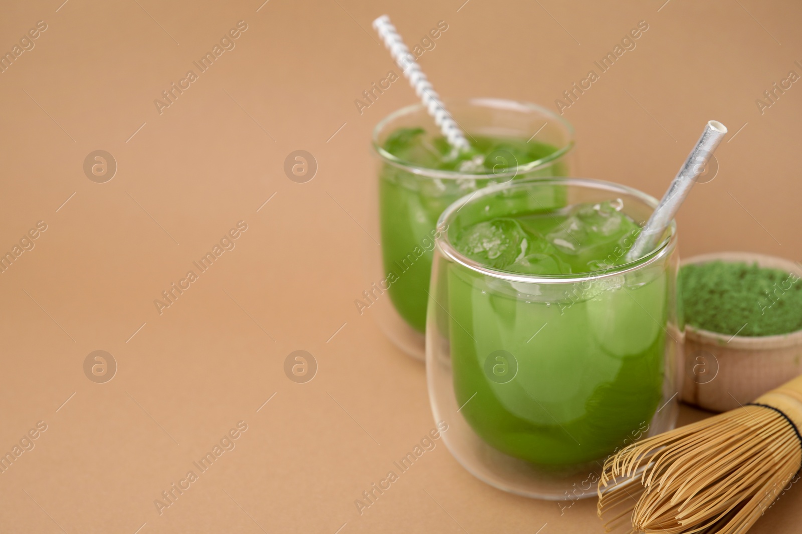 Photo of Delicious iced green matcha tea, powder and bamboo whisk on pale brown background, space for text