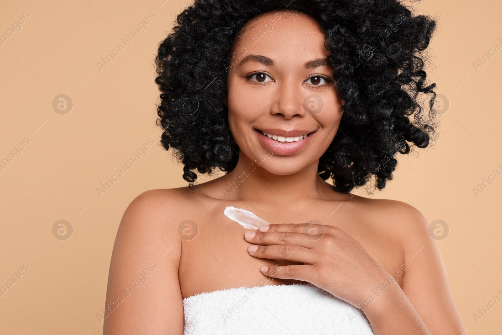 Photo of Young woman applying cream onto body on beige background