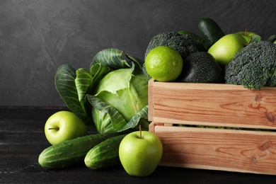 Wooden crate, fresh green fruits and vegetables on dark background