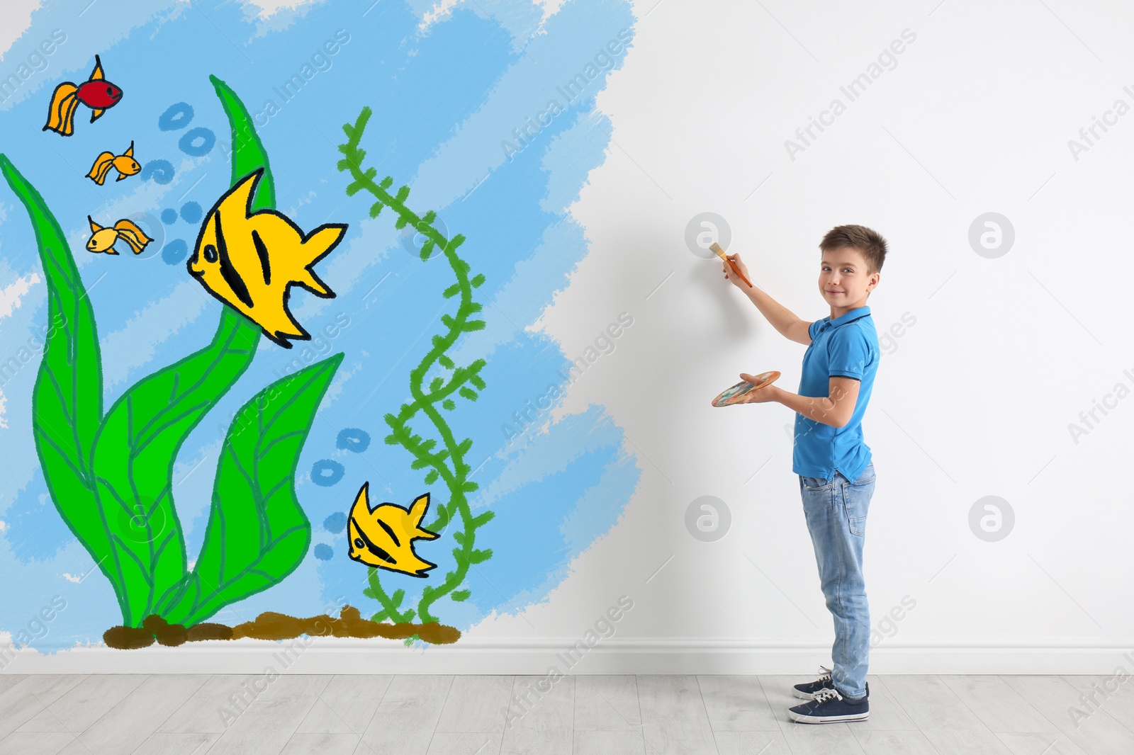 Image of Cute child drawing sea with tropical fishes on white wall indoors