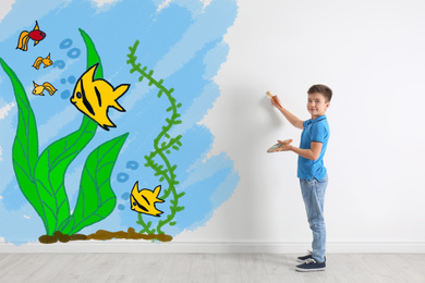 Image of Cute child drawing sea with tropical fishes on white wall indoors