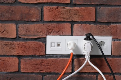 Photo of Many different electrical power plugs in sockets on red brick wall, space for text