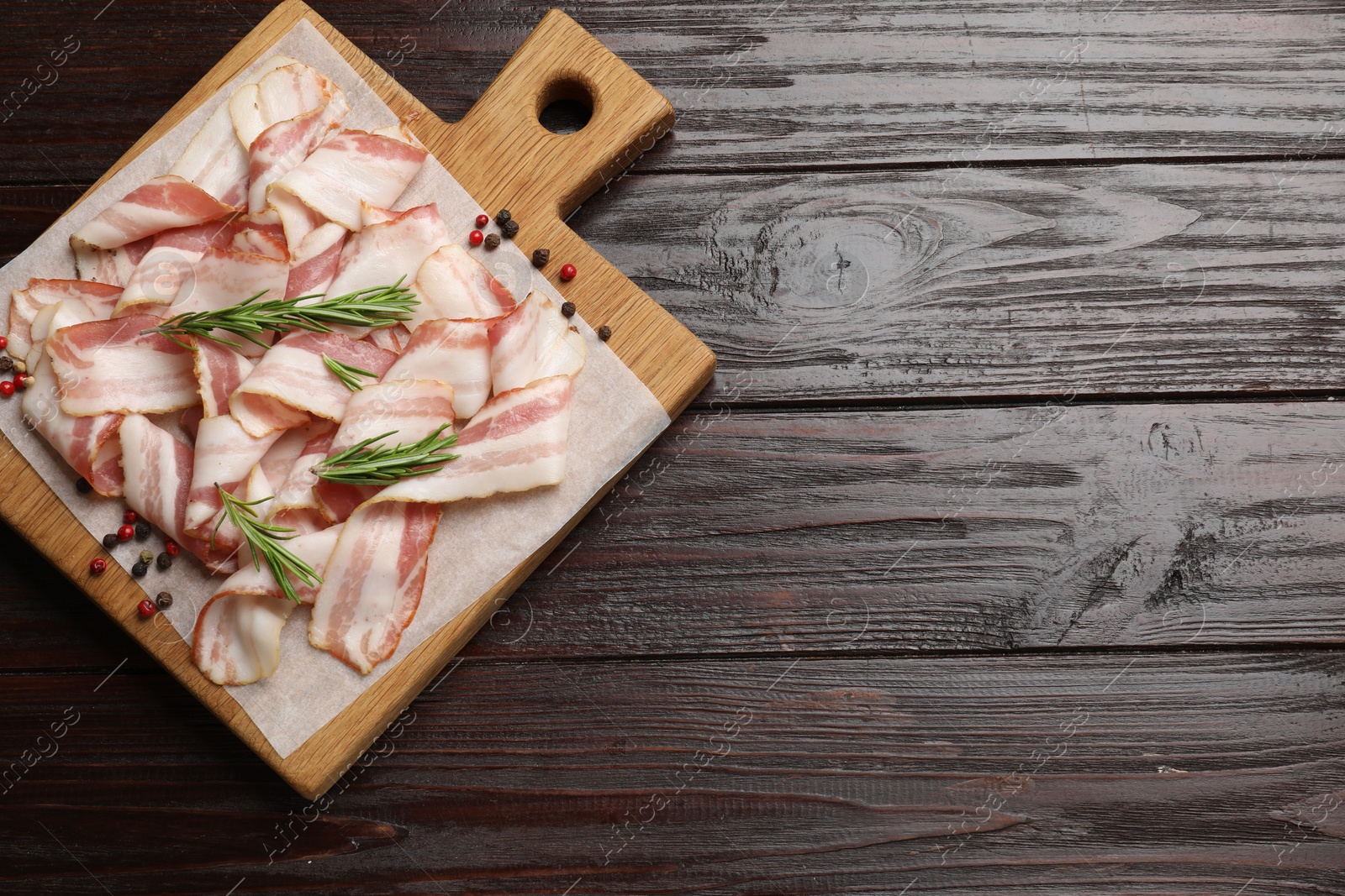 Photo of Slices of raw bacon and spices on wooden table, top view. Space for text