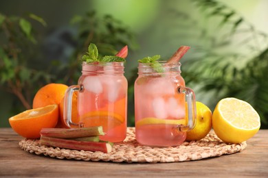 Mason jars of tasty rhubarb cocktail with citrus fruits on wooden table outdoors